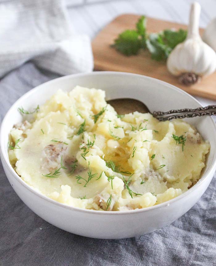 Mashed potatoes in a white bowl with butter and fresh dill