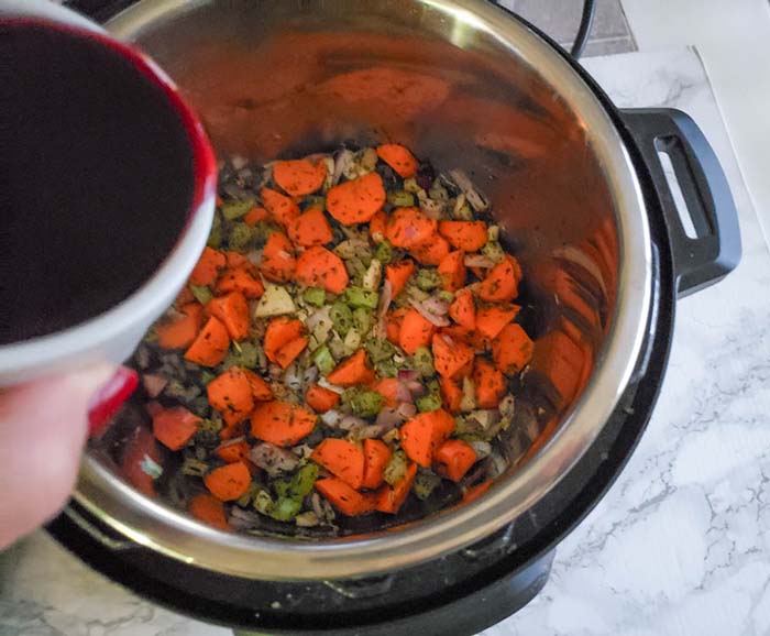 Red wine pouring from a white cup into vegetables in Instant Pot