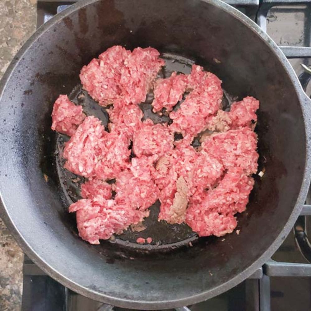 beer chili process step 1, ground beef cooking in a cast iron pan