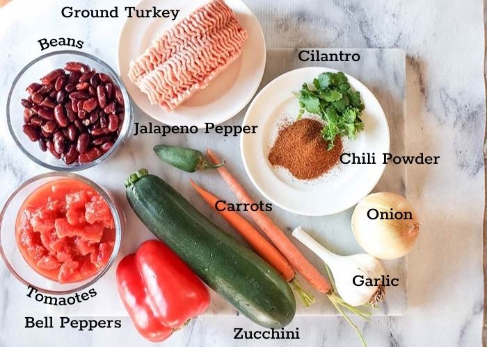 Ingredients for turkey chili with ground turkey, cilantro, chili powder, onion, garlic. carrots, jalapeno pepper, zucchini, tomatoes, bell peppers, beans