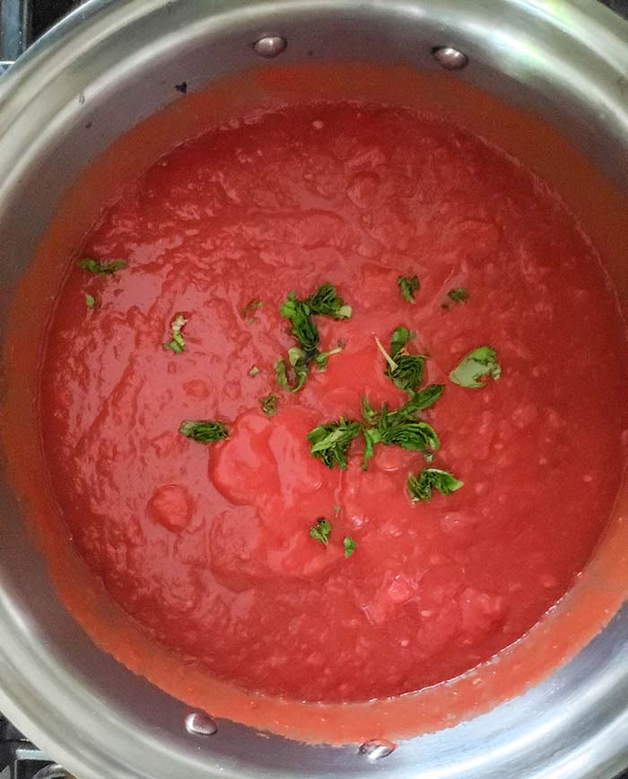 marinara sauce coking in a pot with herbs on top