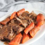 a white platter filled with slices of pot roast and carrots