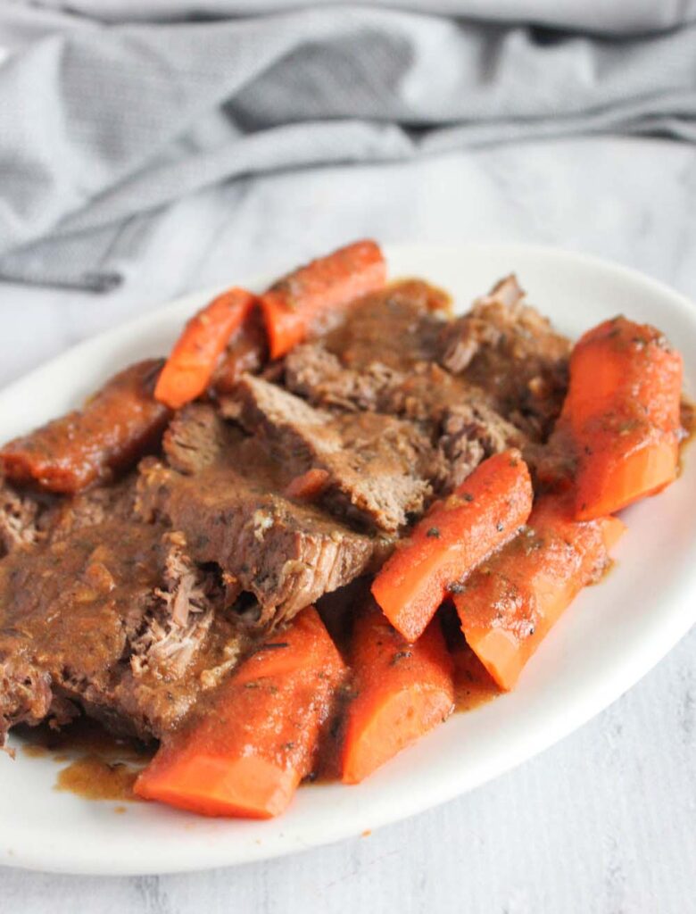 a white platter filled with slices of pot roast and carrots