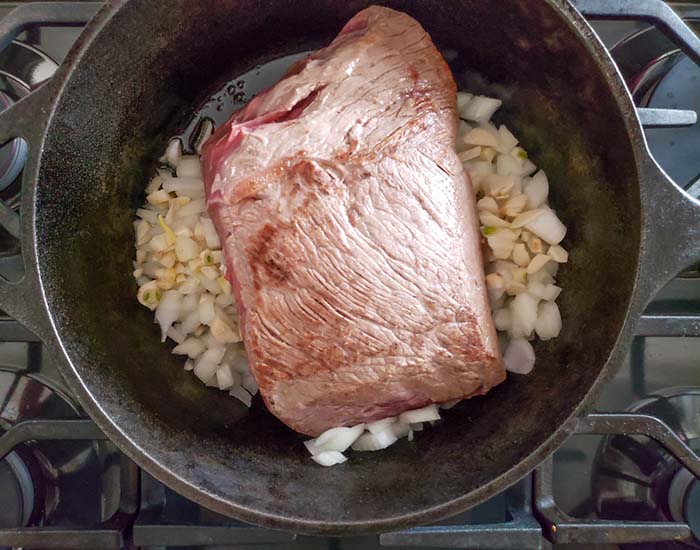 beef roast cooking with garlic and onions in a dutch oven