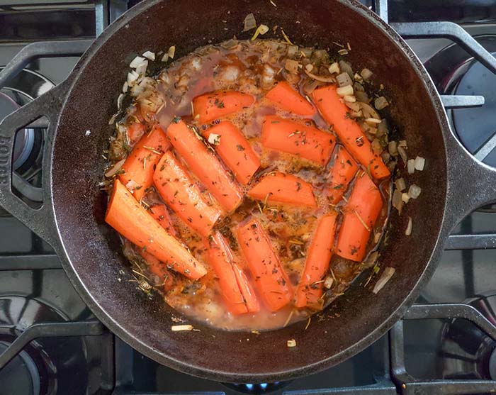 Carrots cooking in a skillet with beer and onions