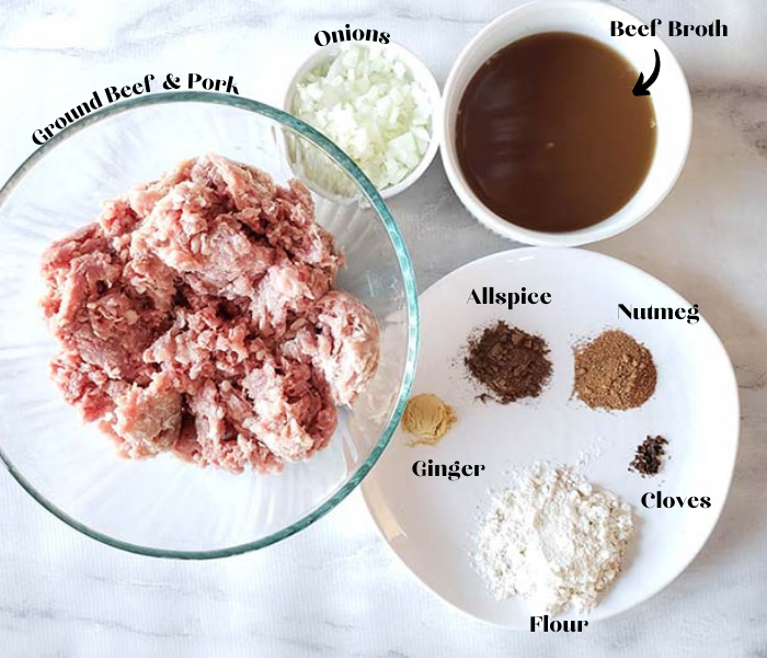 overhead view of ingredients in bowls to make Swedish meatballs including ground beef and pork, onions, beef broth, and spices on a white plate 