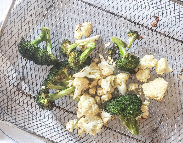 cooked broccoli and cauliflower on an air fryer tray