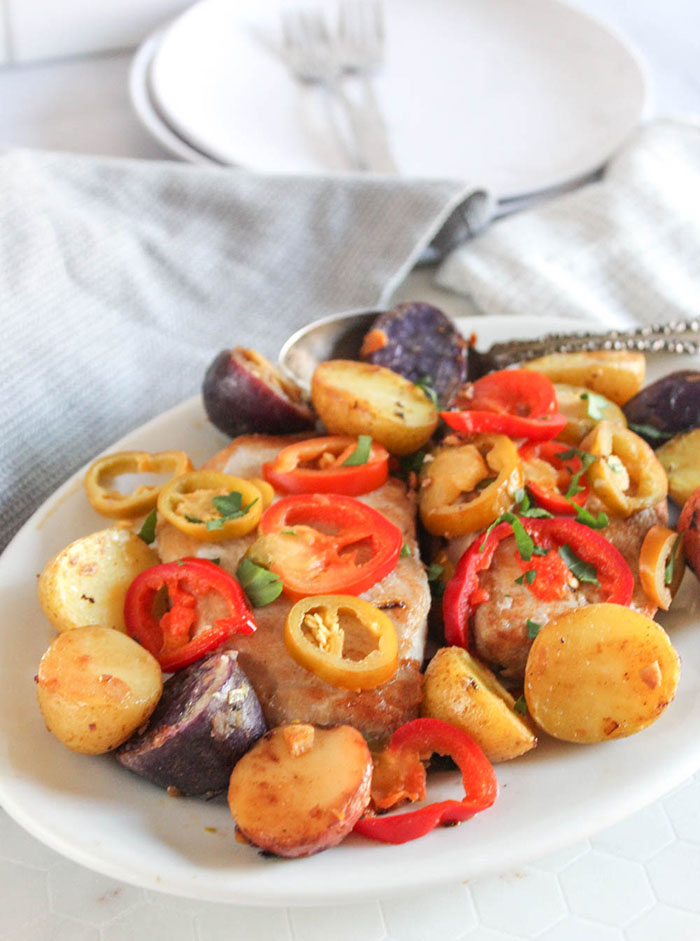 a close up picture of pork chops potatoes and peppers on a white platter