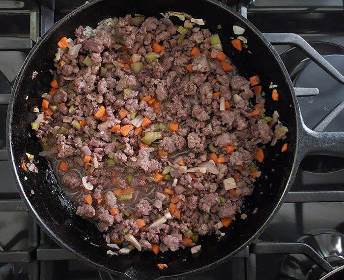 Ground beef cooking on medium in pan with garlic, onions, celery and carrots.