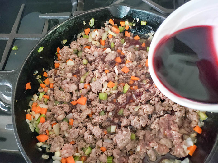Ground meat and vegetables with wine pouring in