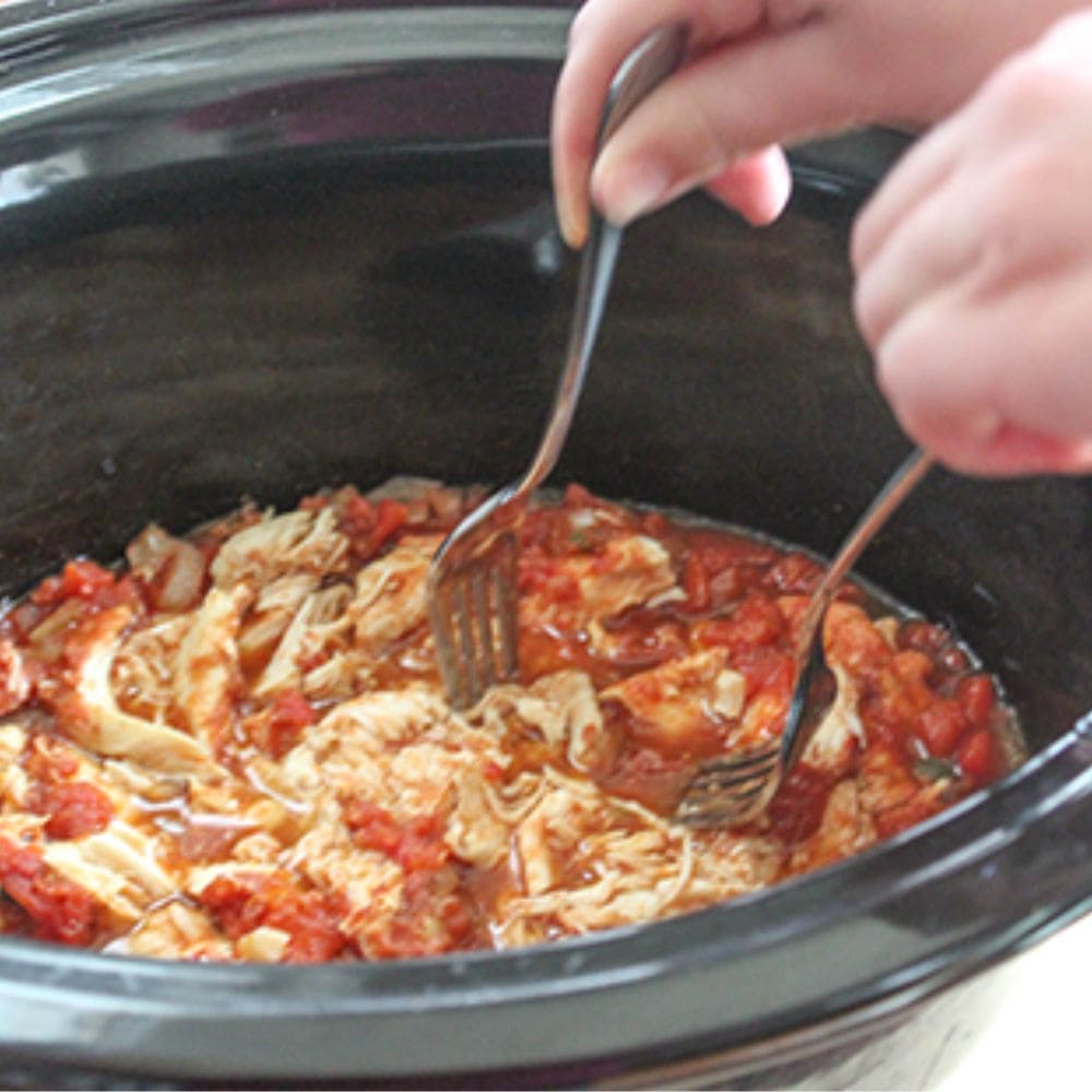Taco chicken process step 3 two forks shredding chicken in a crockpot