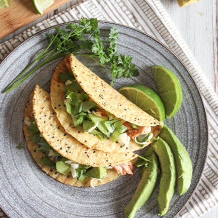 an overhead view of chicken tacos on a plate with avocado slices