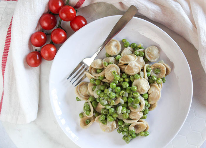 an overhead view of pasta and peas on a plate with a fork