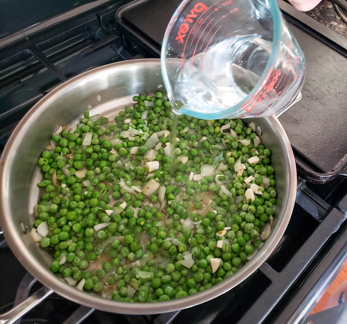 Peas and pasta process water being added to peas in skillet