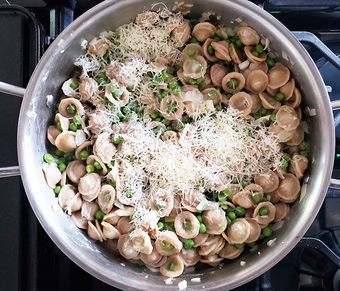 an overhead view of pasta and peas in a pan with cheese on top