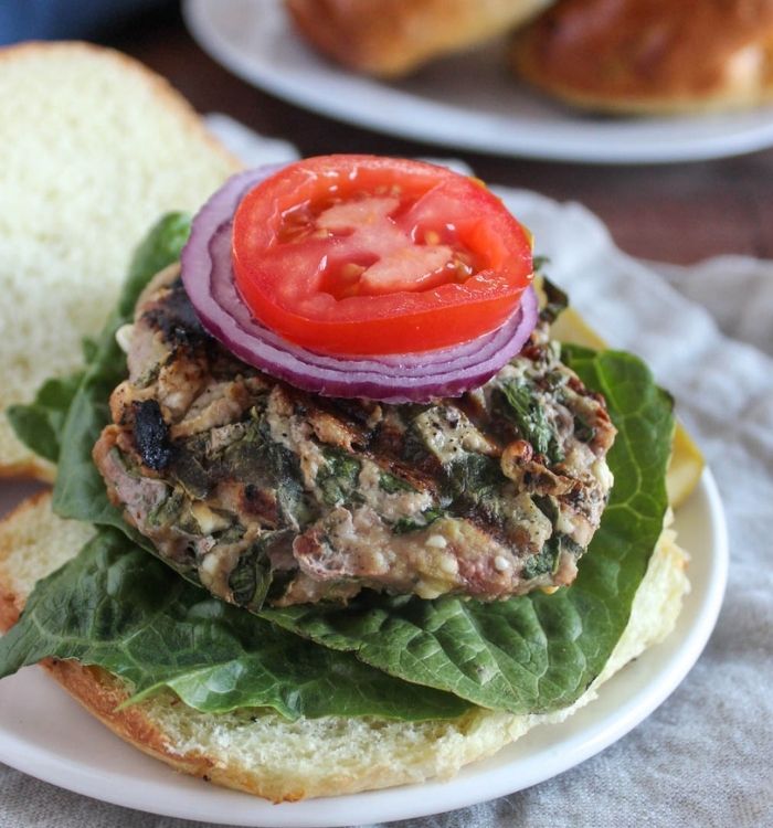 turkey burger made with spinach and feta on a roll with red onion and tomato on top