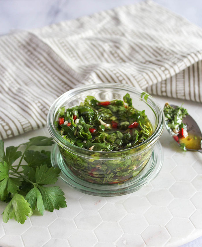 chimichurri sauce in a jar with a spoon on the side