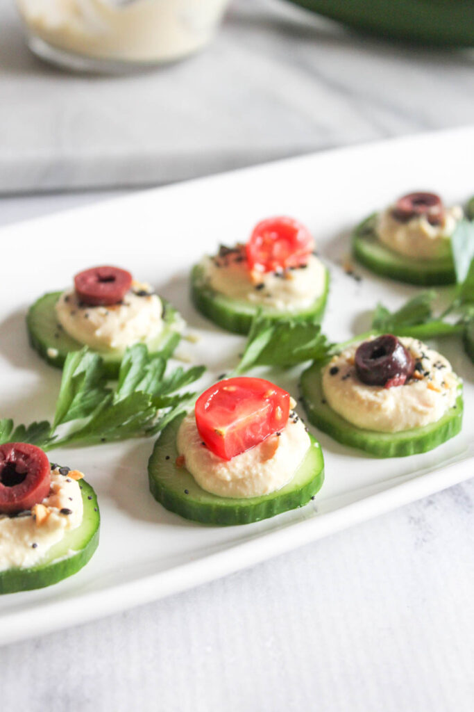 a close of cucumber slices with hummus and toppings on a plate