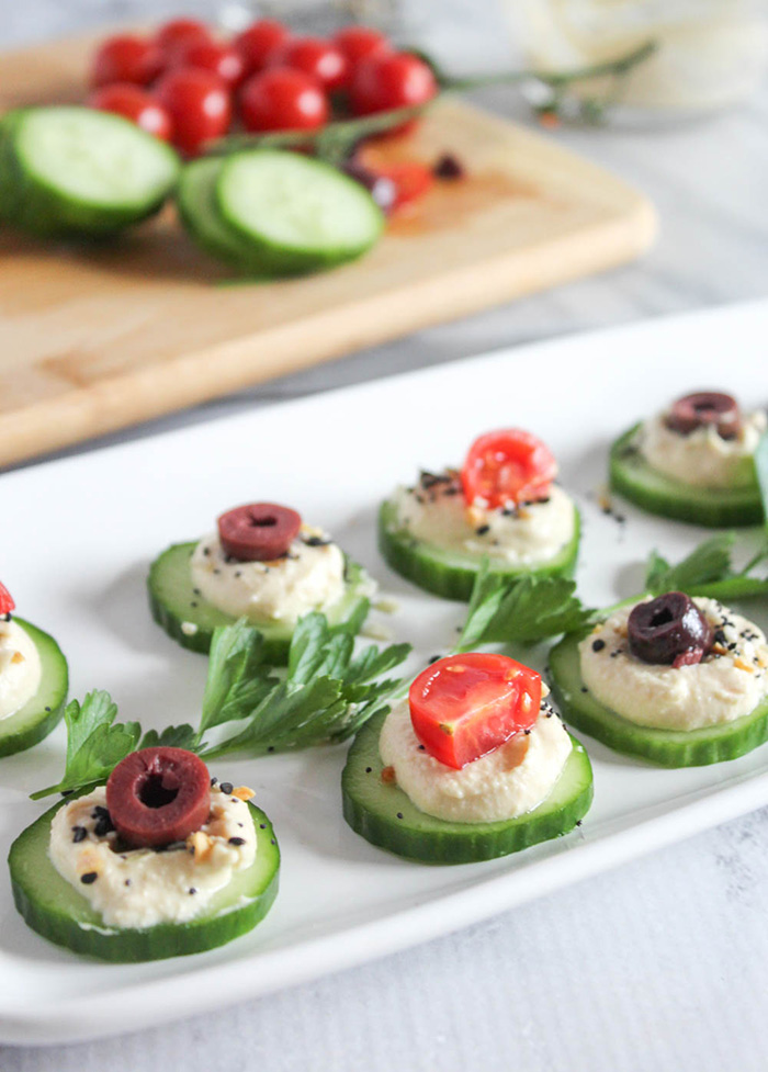 cucumber slices on a plate with hummus and olives on top