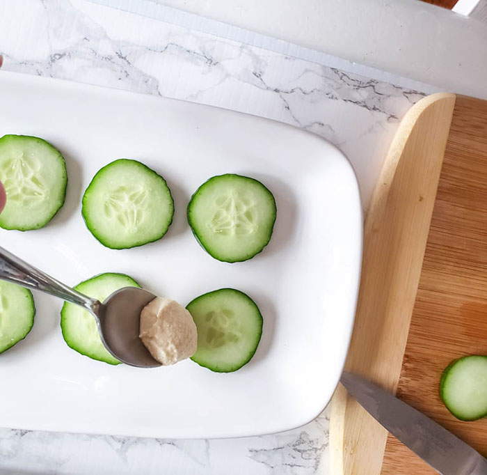 cucumber slices on a plate with a spoon adding hummus