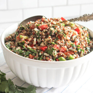 A close up picture of quinoa salad in a white bowl with a spoon