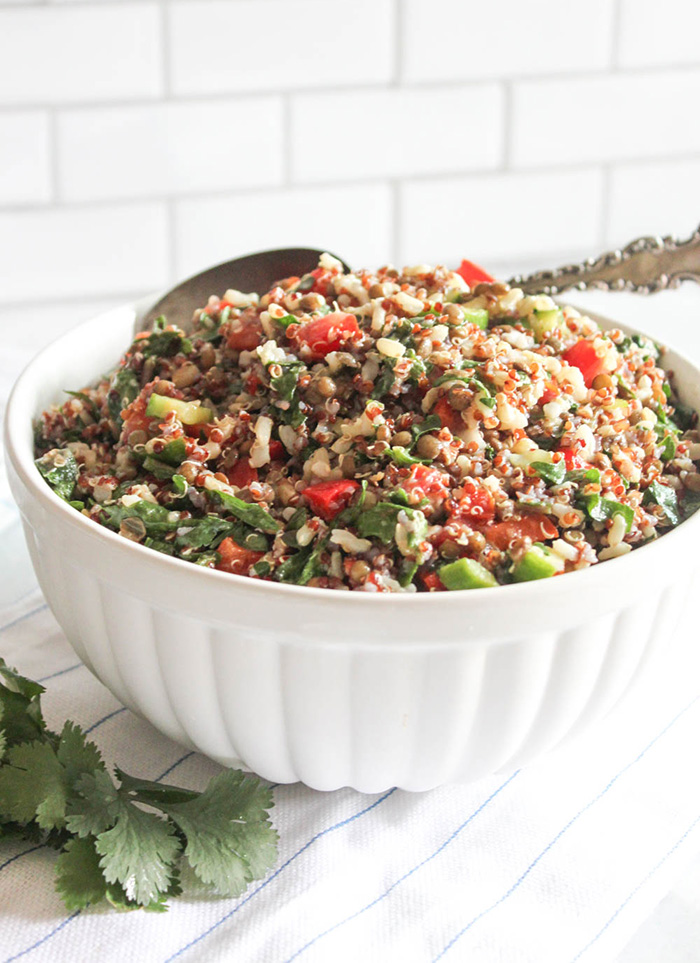 A close up picture of quinoa salad in a white bowl with a spoon