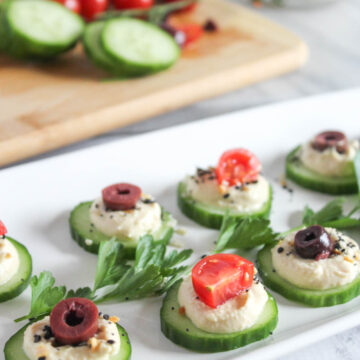 cucumber slices on a plate with hummus and olives