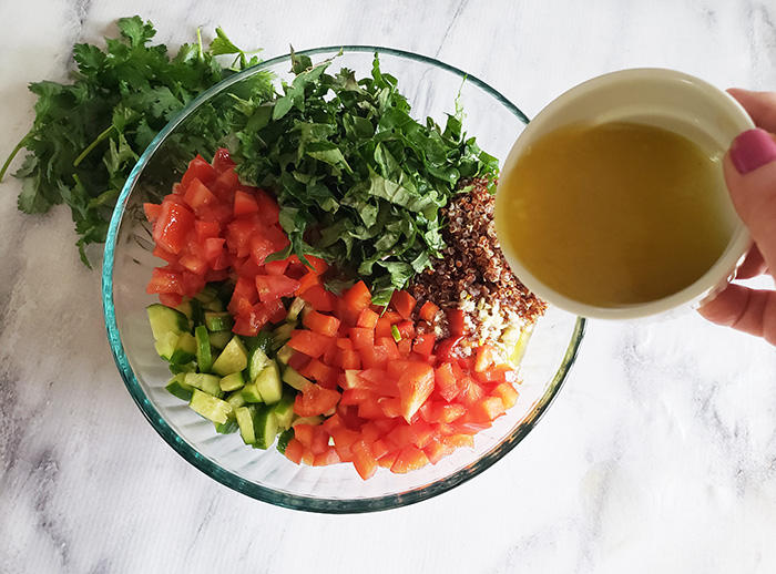 quinoa salad ingredients in bowl adding dressing