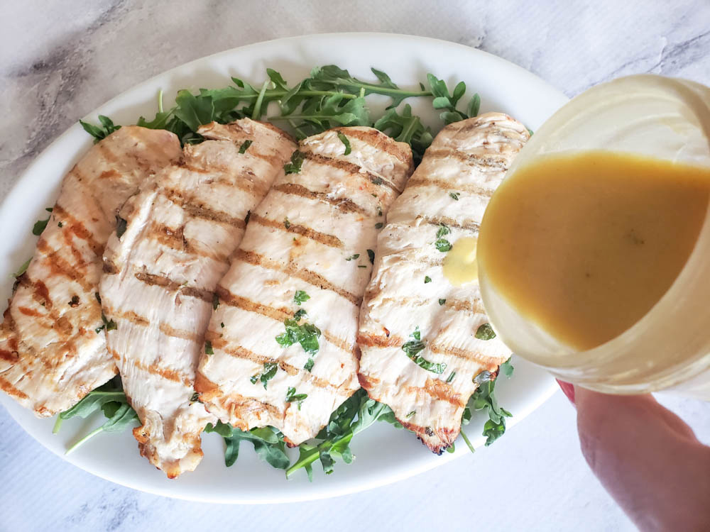 pouring lemon sauce over chicken cutlets