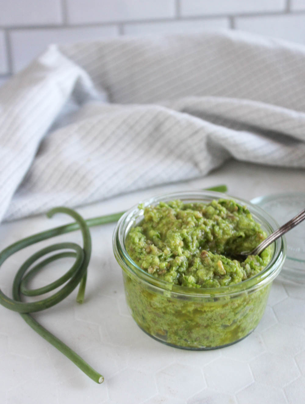 Garlic pesto in a jar with a garlic scape next to it