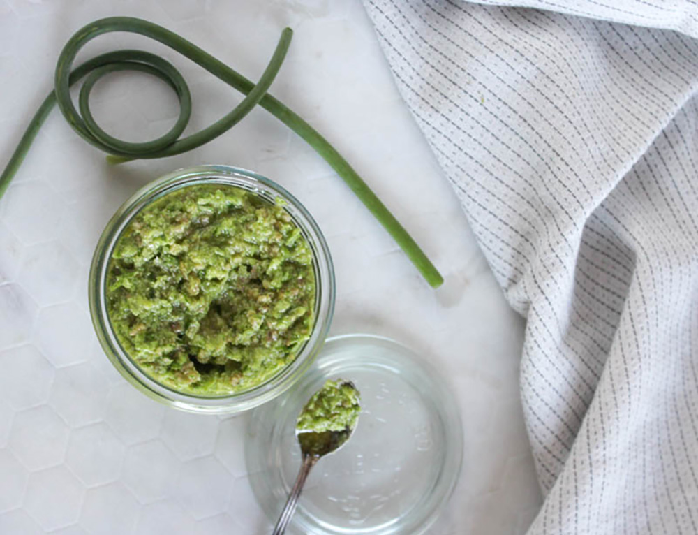 overhead view of garlic scape pesto sauce in a jar with a spoon on the side