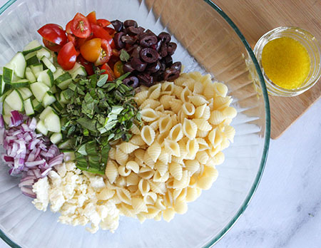 an overhead view of Greek pasta salad ingredients in a bowl