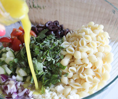 An overhead view of lemon dressing pouring into pasta salad