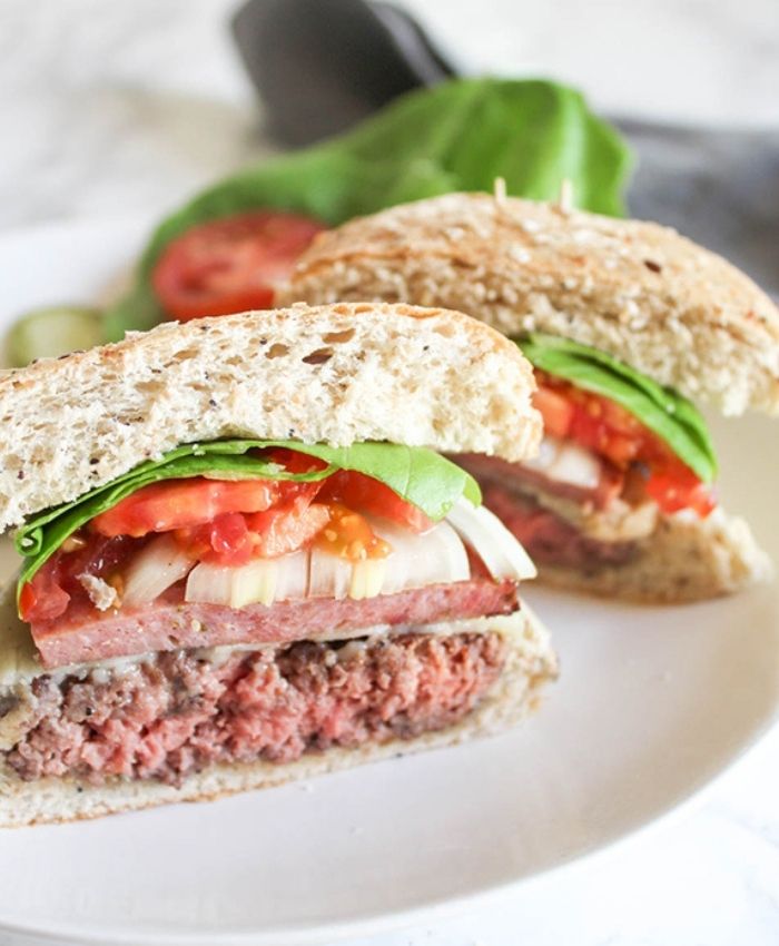 a photo of a burger cut in half on a plate with lettuce tomato and onions