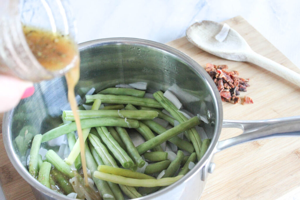 green beans in a pan with dressing being added