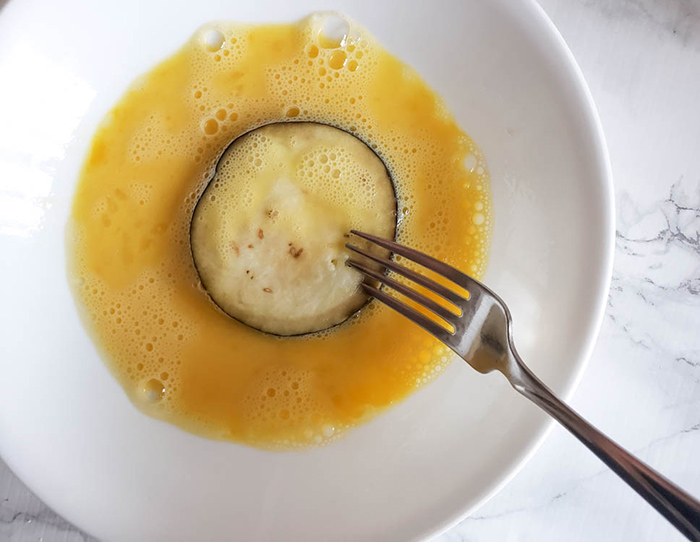 eggplant slice dipped into egg wash with a fork