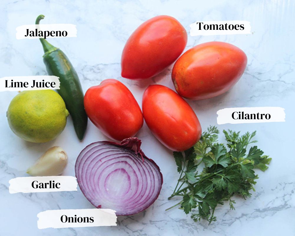 Ingredients to make salsa with roma tomatoes, jalapeno, lime, garlic, red onion sliced in half and cilantro.