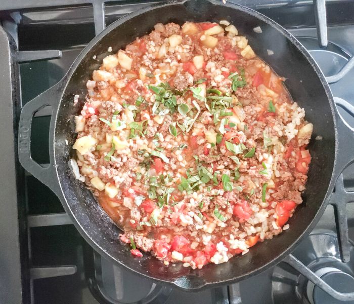 meat rice tomatoes and herbs cooking in a skillet on the stove