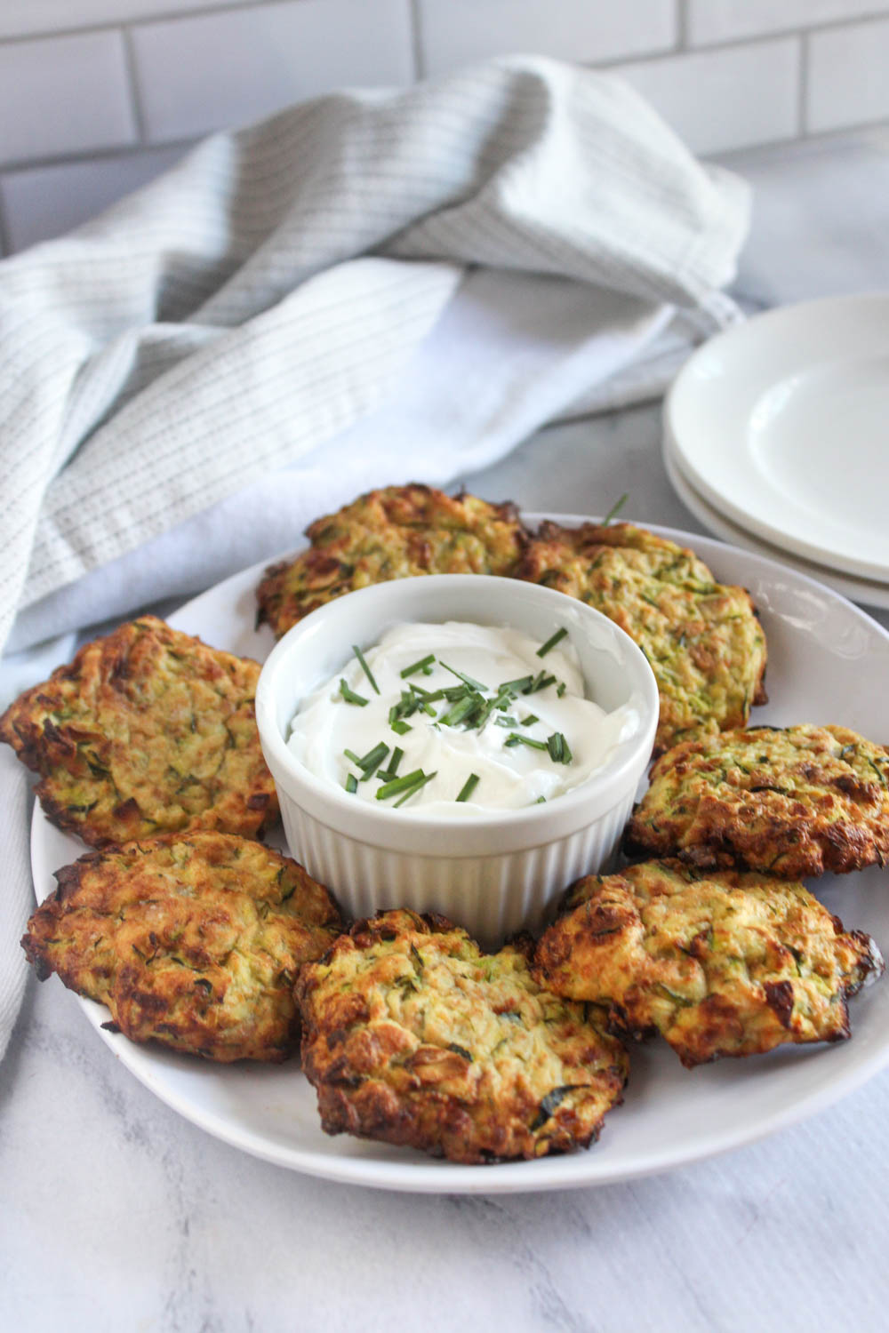 zucchini fritters on a white plate with a small bowl of sour cream in the center