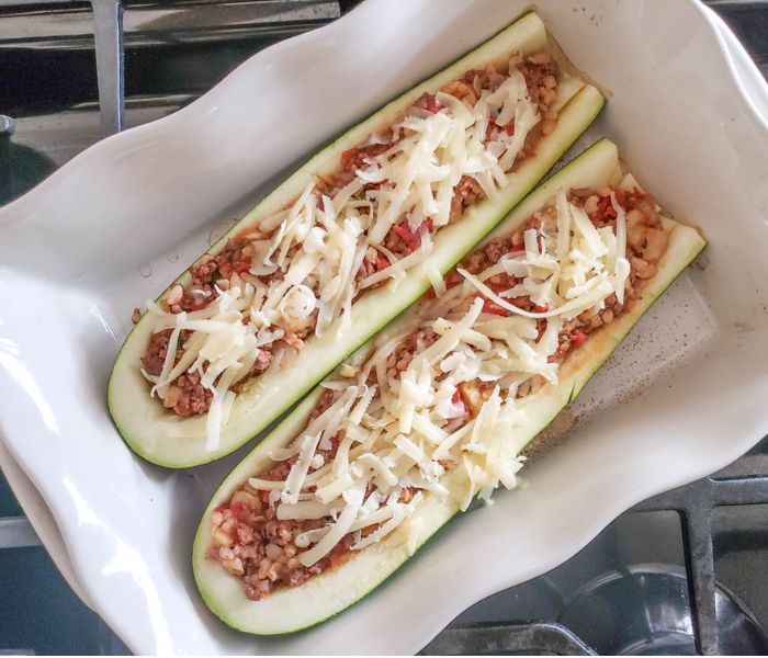 stuffed zucchini in a baking dish with unmelted shredded cheese