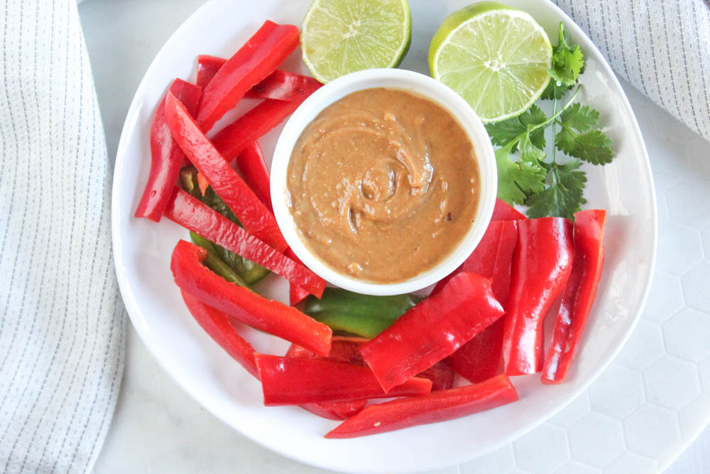 overhead view of peanut sauce in a white plate with red and green peppers