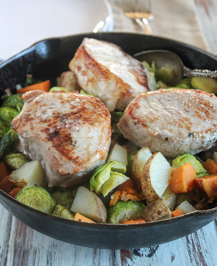 pork chops in a pan with vegetables and a spoon