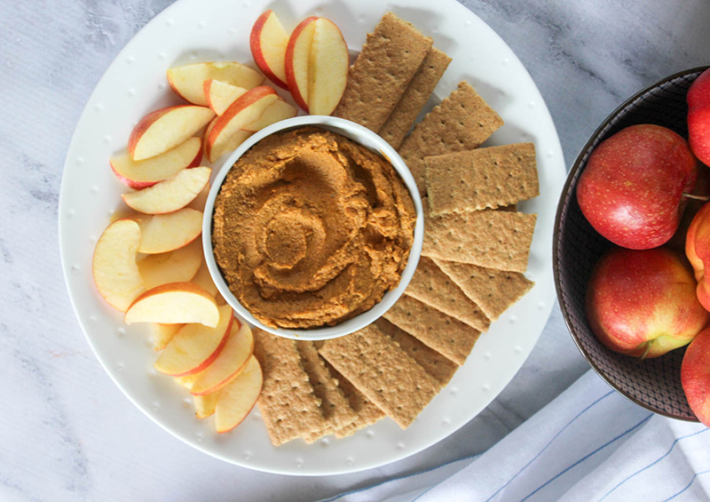 overhead view of pumpkin pie hummus on a plate with apple slices and crackers