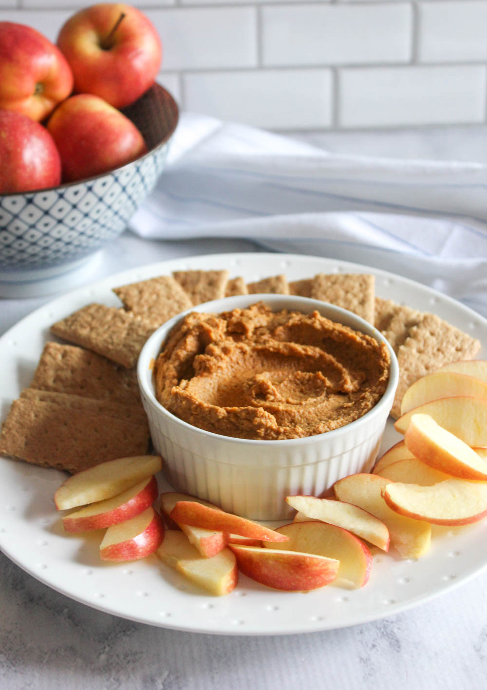 pumpkin pie hummus on a plate with sliced apples and crackers with apples in the background