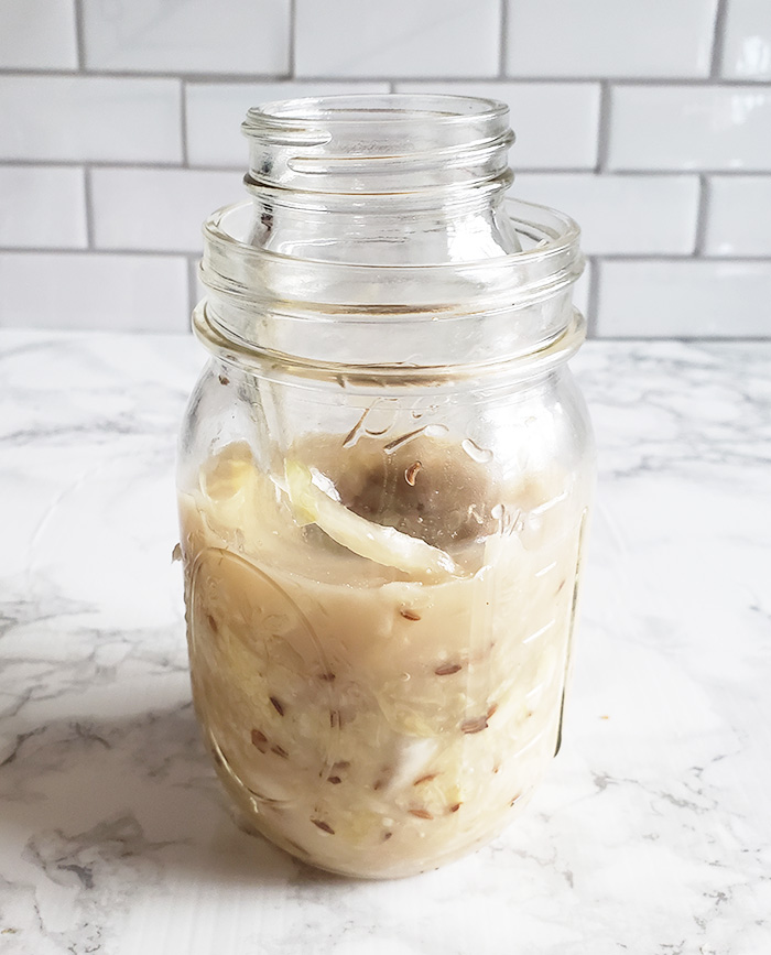 This photograph shows the step four of how to make sauerkraut in jar. Smaller jar is pressing cabbage down in bring in larger jar.