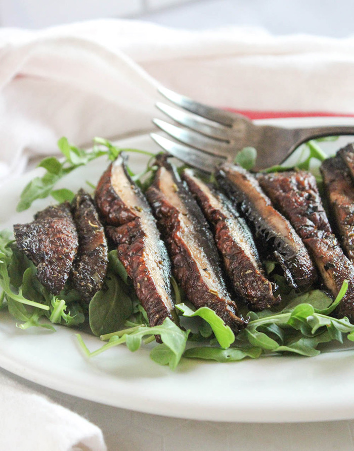 A close up picture of sliced air fryer portobello mushrooms on a platter with arugula