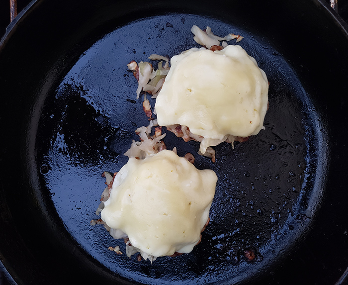 process of turkey burgers cooking in a pan with cheese and sauerkraut