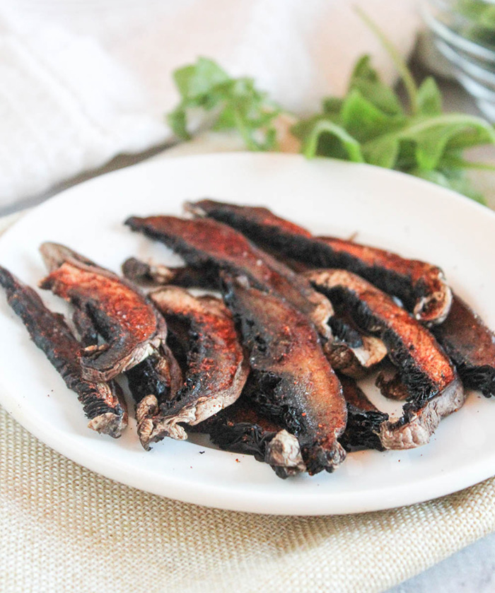 slices of mushroom bacon on a white plate with lettuce in the backgroudn