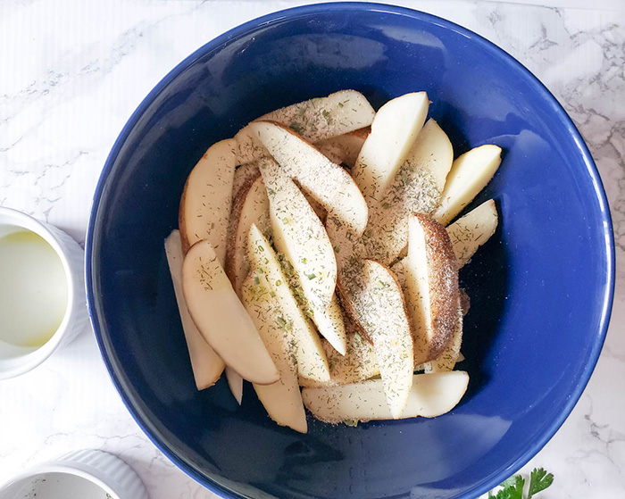 potato wedges in a blue bowl with oil and seasoning on them