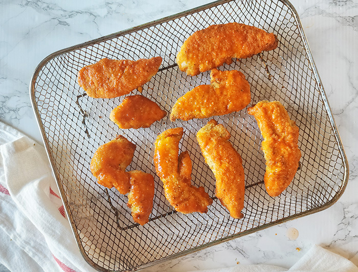 Buffalo chicken tenders on an air fryer tray covered with buffalo sauce